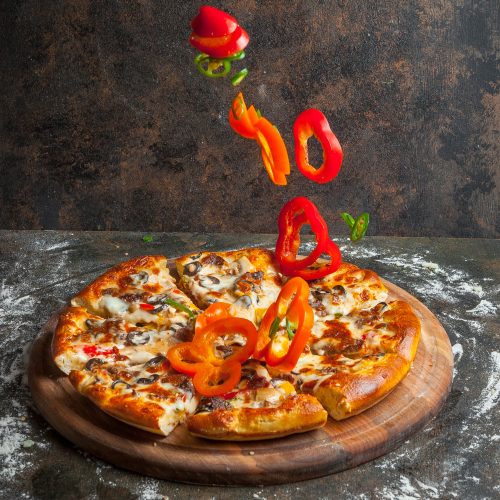 Side view pizza with slices of bell pepper and pizza slices and flour in board cookware on stone background